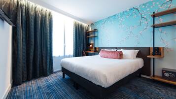 A hotel room with a large bed, a blue patterned carpet, a window with curtains, and a wall with a cherry blossom mural.