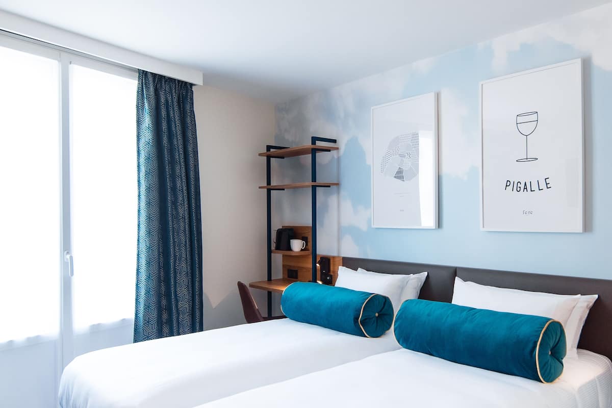 Habitación de hotel con cama, escritorio y silla. La cama tiene dos almohadas y una ventana con cortinas.