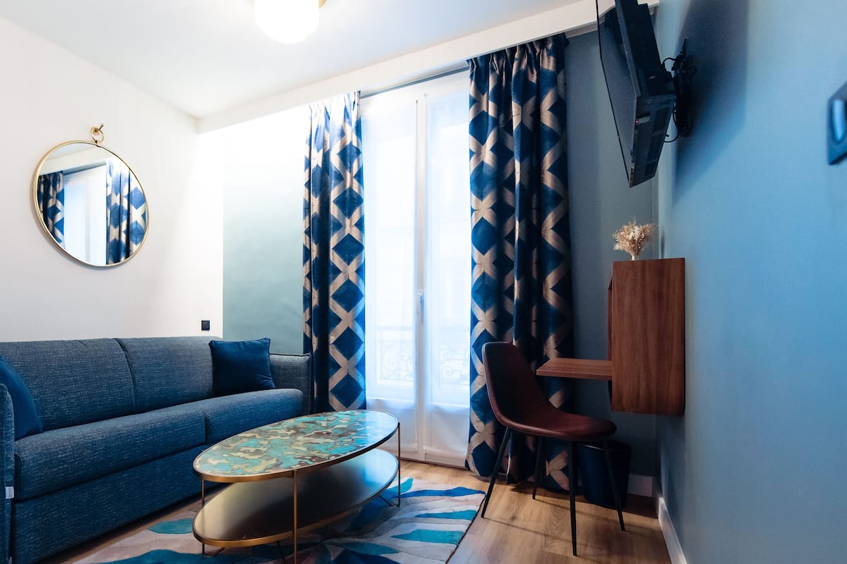 Una sala de estar moderna con un sofá azul, un espejo redondo, una mesita y una silla.