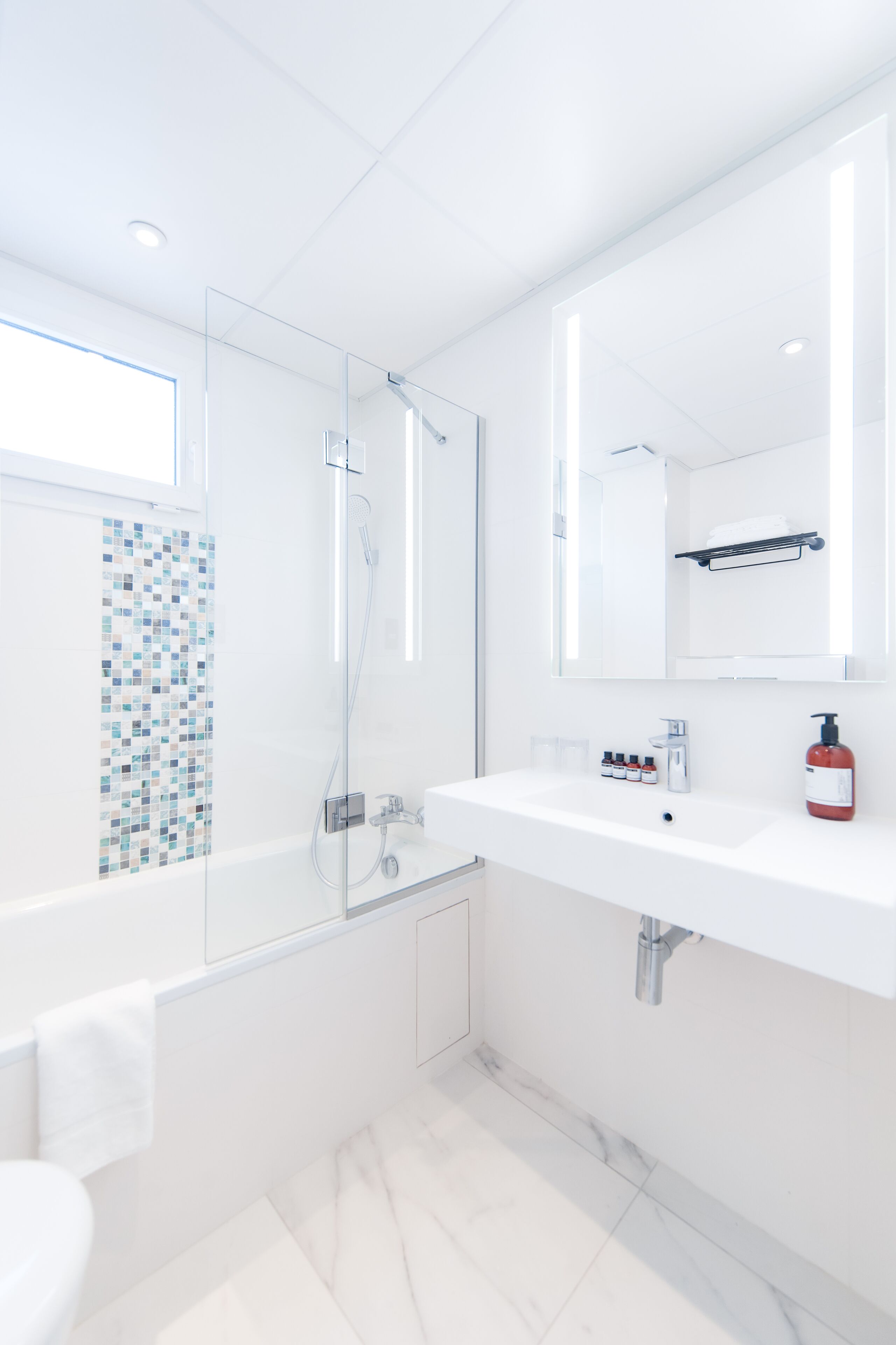 A modern bathroom with a glass shower enclosure, a white sink with a mirror above, and a tiled backsplash.