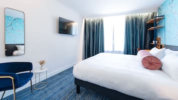 Une chambre d’hôtel avec un lit, une télévision, une chaise, une petite table et une fenêtre avec des rideaux.
