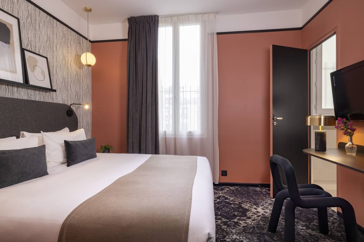 A hotel room with a large bed, a desk with a chair, a television, and a window with curtains.