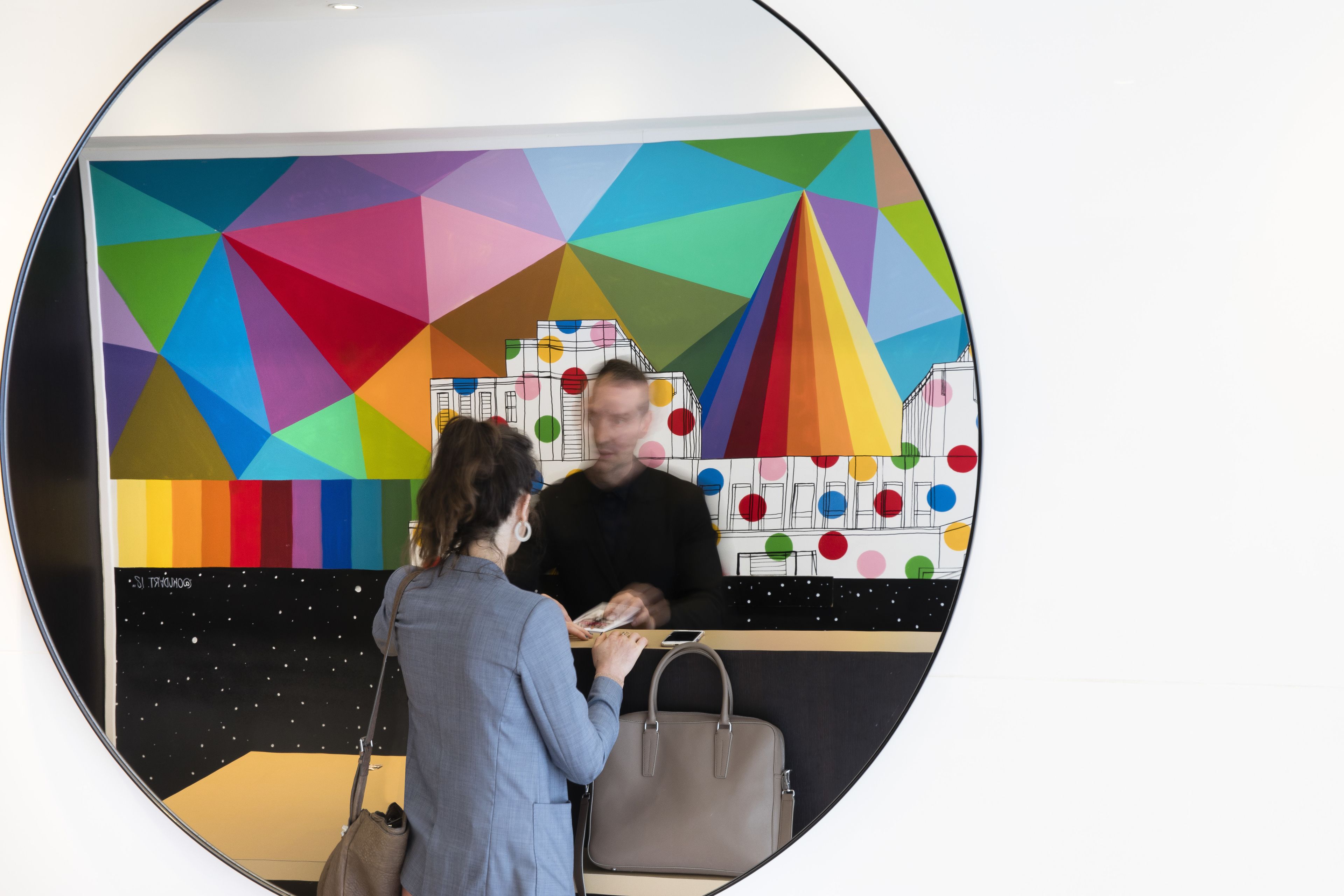 Une vue circulaire d’une pièce avec un mur orné d’un motif géométrique, une grande fenêtre et une porte bien visible.