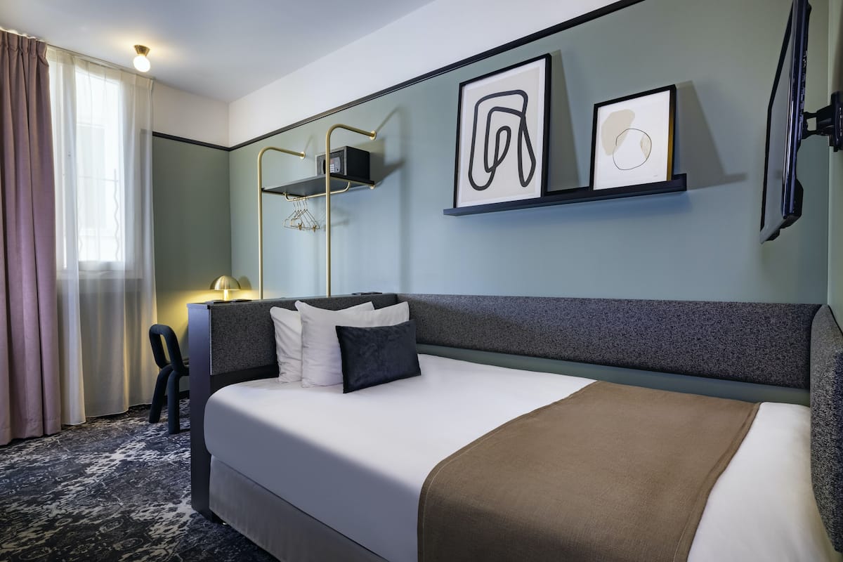 A hotel room with a large bed, a desk, a chair, a TV, and artwork on the wall.