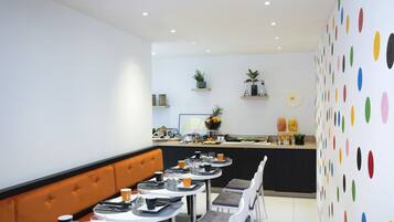 A modern dining area with round tables, cushioned booths, and a kitchen counter with various items.