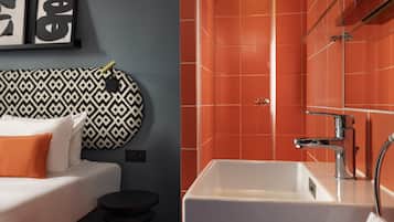 A hotel room with a bed, a bedside table, a small stool, a white sink with a chrome faucet, and orange tiled walls.