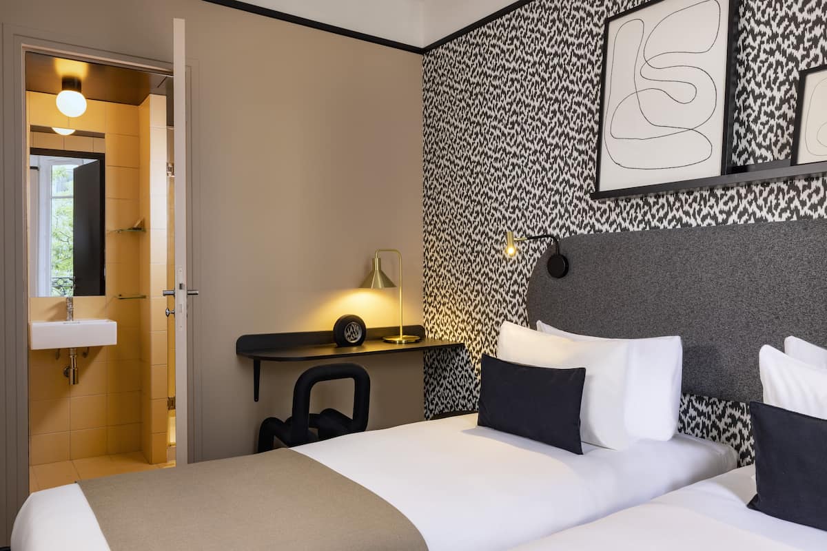 A hotel room with a bed, bedside table, lamp, and a wall with a patterned design.
