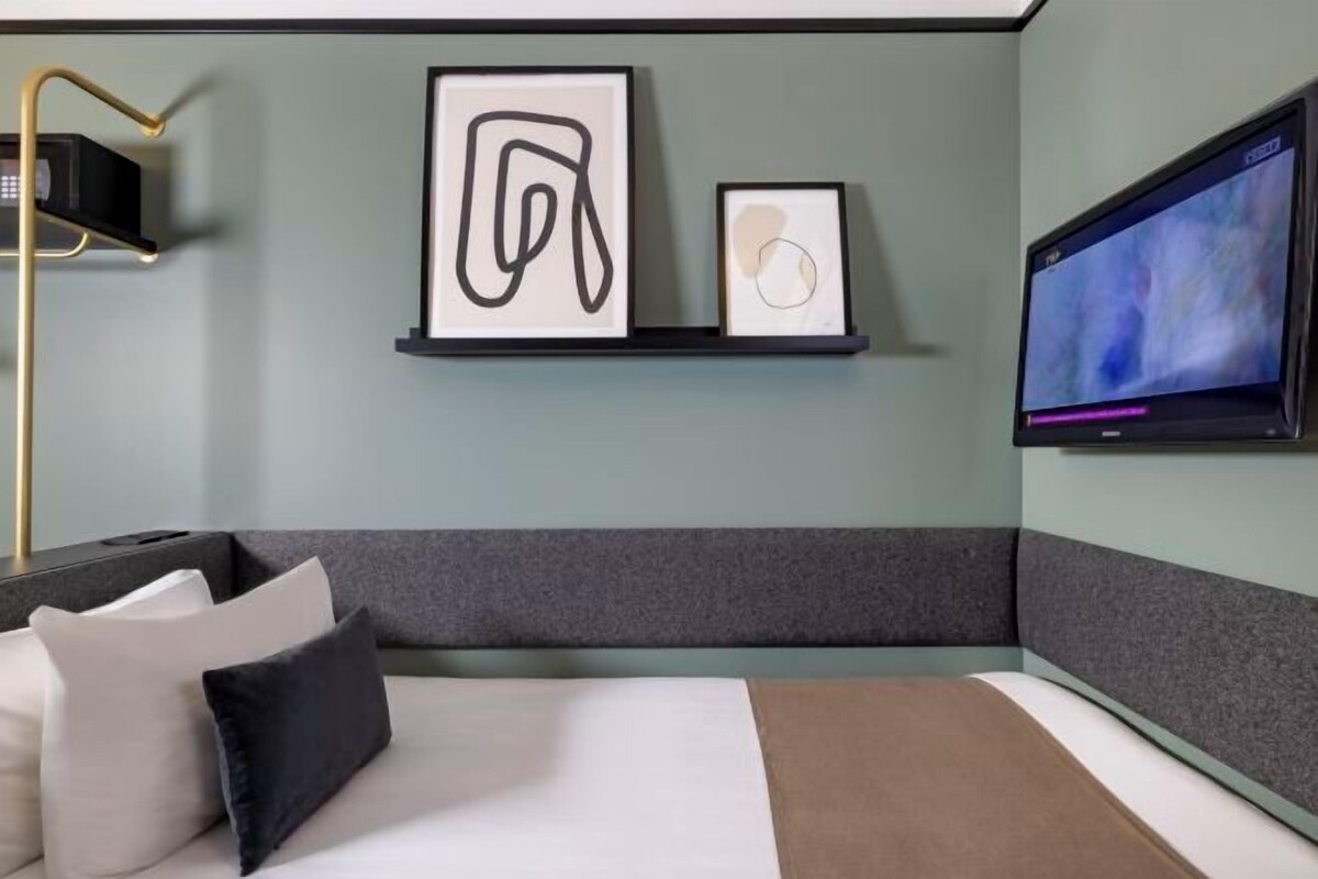 A modern hotel room with a bed, a flat-screen TV, and artwork on the wall.