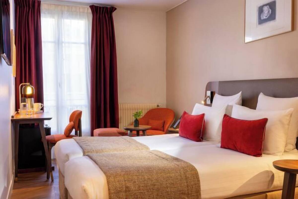 A hotel room with a large bed, a desk with a lamp, a chair, and a small table.