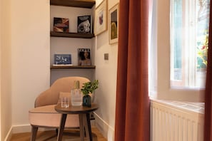 A corner room with a chair, a small table with a vase and a glass, and shelves with books and framed pictures. - Europe Hotel Paris Eiffel (Paris)