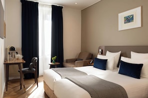 A hotel room with a large bed, a desk with a lamp, a chair, and a small table with a plant. - Europe Hotel Paris Eiffel (Paris)
