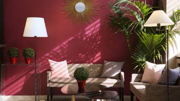 Een moderne woonkamer met een rode muur, een ronde spiegel, twee potplanten, een bank en twee vloerlampen.