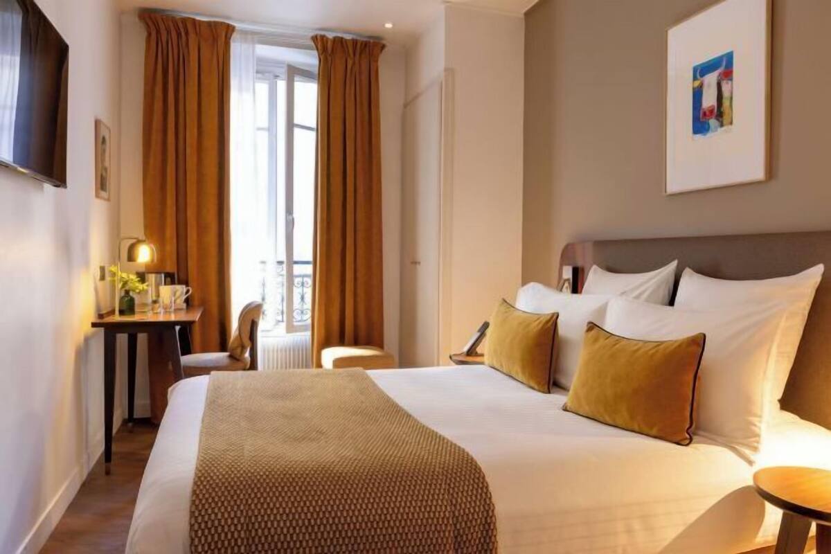 A hotel room with a large bed, a desk with a lamp, and a view of the outdoors.