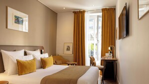 Una camera d'albergo con un letto, una scrivania, una sedia, una finestra con tende e una televisione appesa al muro.