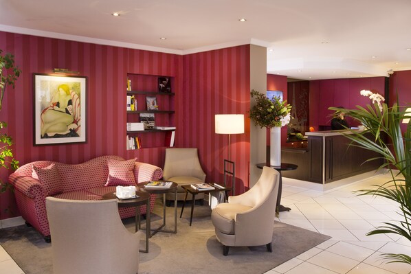 Un vestíbulo de hotel con pared a rayas rojas, un sofá, una silla, una mesita y una recepción.