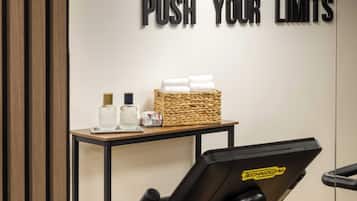 A gym area with a motivational sign, a water bottle, a bottle of lotion, and a basket of towels on a table.