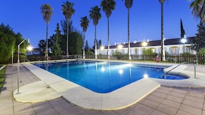 Una piscina con borde de baldosas, rodeada de palmeras y una valla.