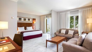 Una habitación de hotel con cama, sofá, mesa de centro, escritorio y lámpara.