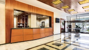 Zona de recepción de hotel con mostrador de madera, suelo de baldosas y un espejo grande.