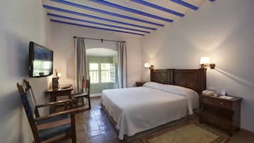 A bedroom with a bed, bedside tables, a chair, a TV, and a window with curtains.