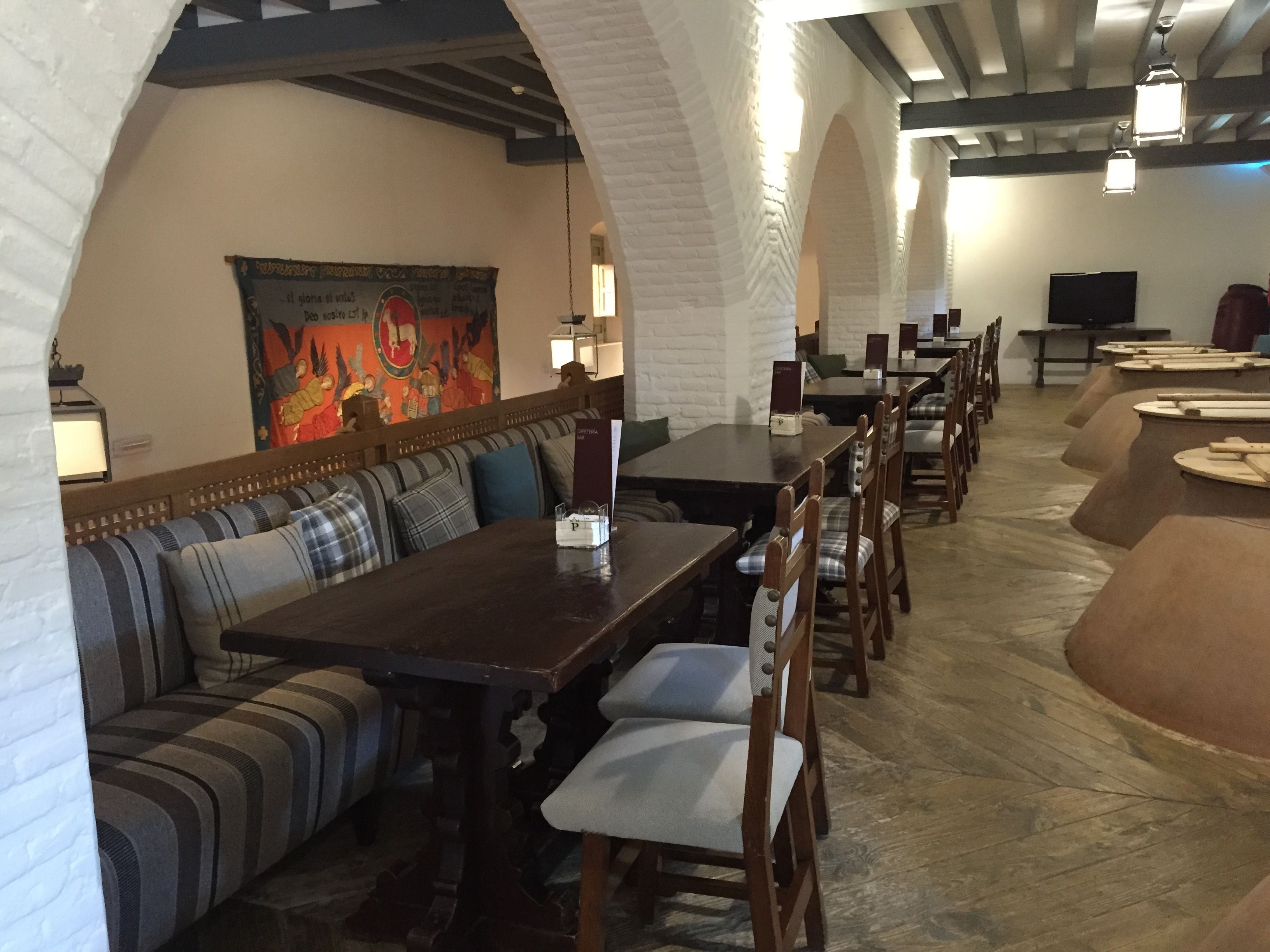 A restaurant with a long wooden table, cushioned seating, and a mural on the wall.