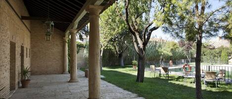 A covered outdoor area with stone columns, a brick wall, and a grassy lawn with trees and outdoor furniture.