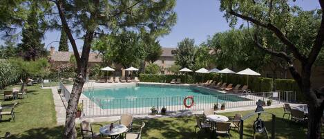 A swimming pool surrounded by lounge chairs and umbrellas, with a grassy area and trees in the foreground.