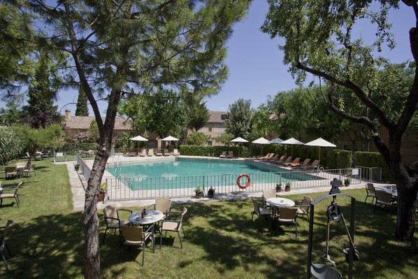 A swimming pool surrounded by lounge chairs and umbrellas, with a grassy area and trees in the foreground. - Parador de Almagro (Almagro)