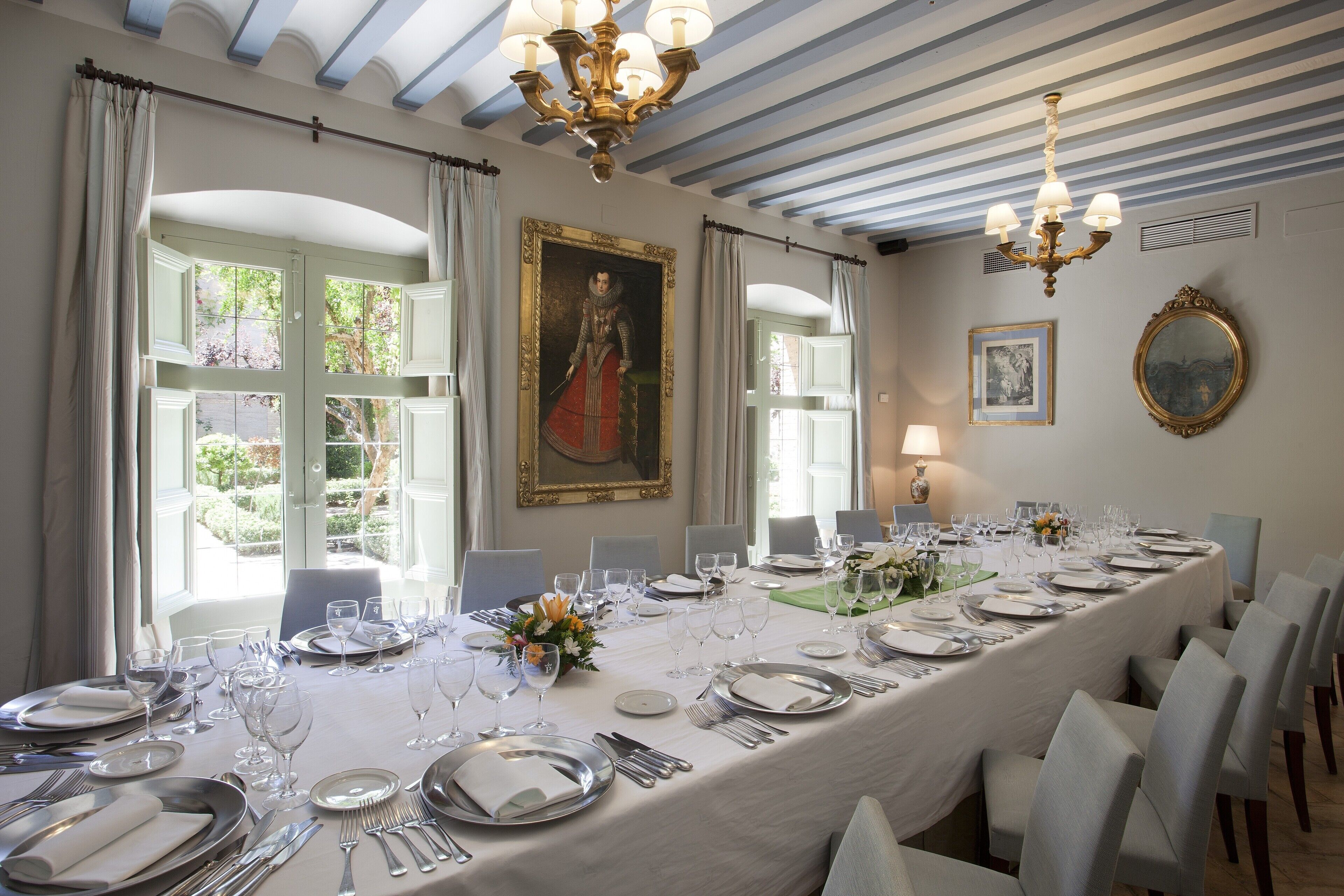 Comedor con una larga mesa dispuesta para una comida, ventanas amplias y una araña.