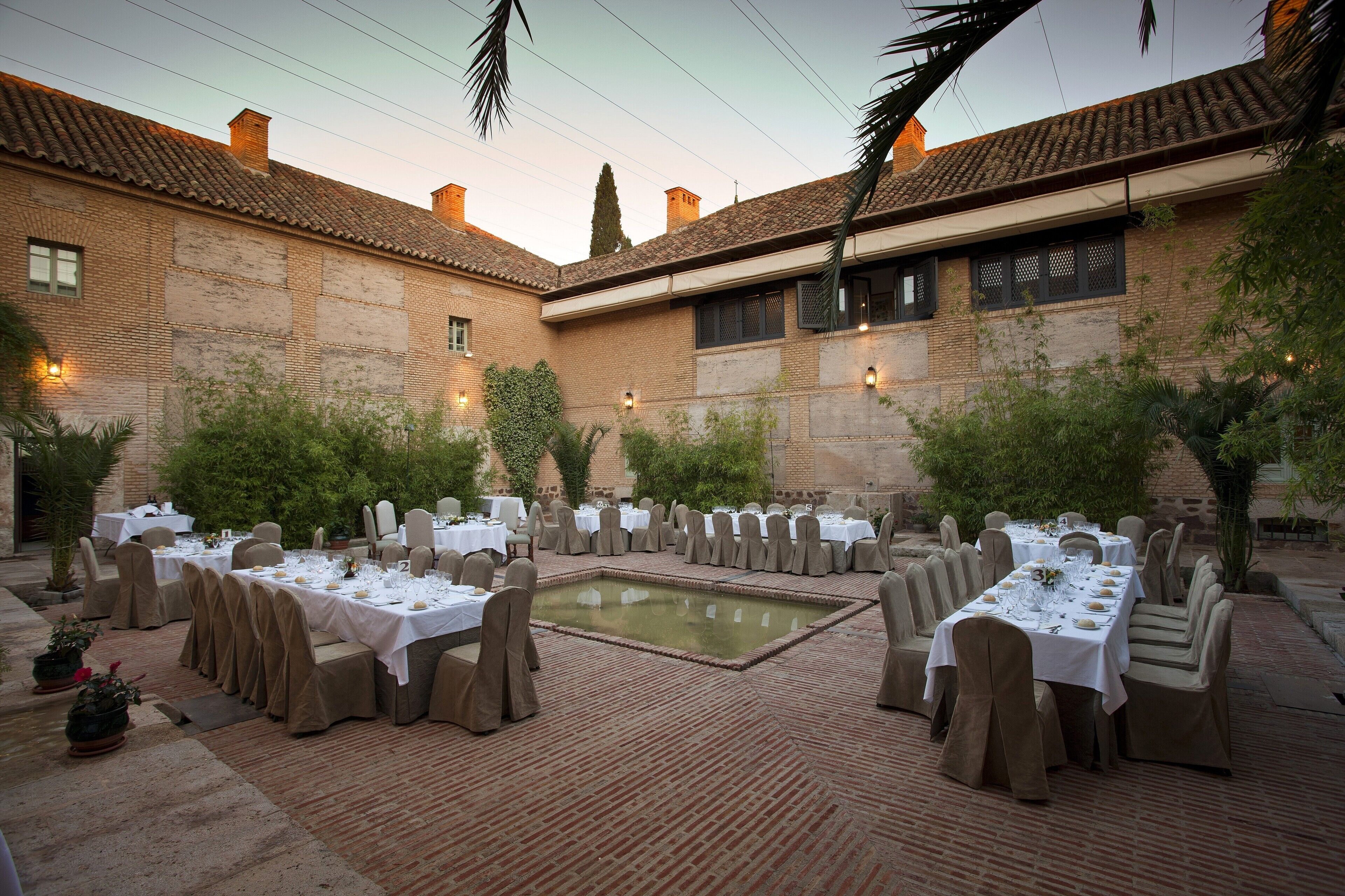 Un área de comedor al aire libre con varias mesas dispuestas para una comida, rodeada de paredes de ladrillo y follaje.