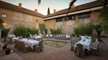 Un área de comedor al aire libre con varias mesas dispuestas para una comida, rodeada de paredes de ladrillo y follaje.
