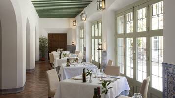 Un restaurante con mesas dispuestas para comer, ventanas amplias y un techo verde.