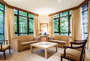 A room with two sofas, a coffee table, and a chair. There are large windows with curtains.
