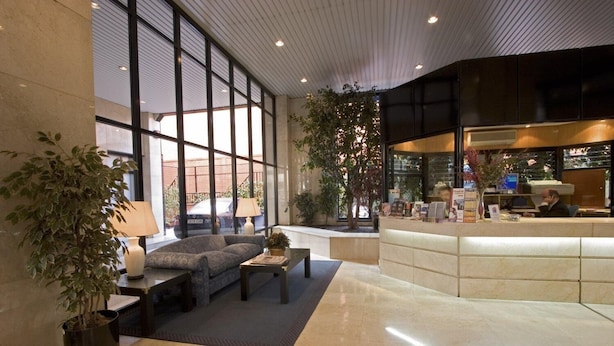 Een moderne lobby met een receptiebalie, een zithoek en grote ramen.