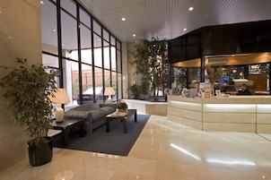 A modern lobby with a reception desk, seating area, and large windows.