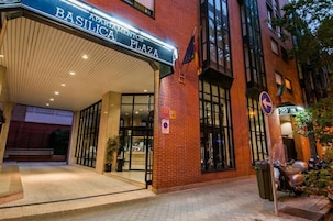 The entrance to the Basilica Plaza apartment building with a clear sign, a flag, and a directional sign.