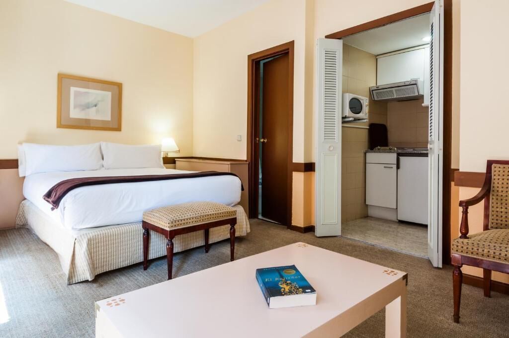 Ein Hotelzimmer mit Bett, Nachttisch, Stuhl und einer kleinen Küchenzeile.