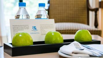 A hotel room with a table set for breakfast, including two water bottles, a plate with two green apples, and a breakfast menu card.