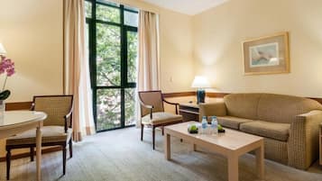 A hotel room with a large window, a sofa, two chairs, a small table, and a lamp.