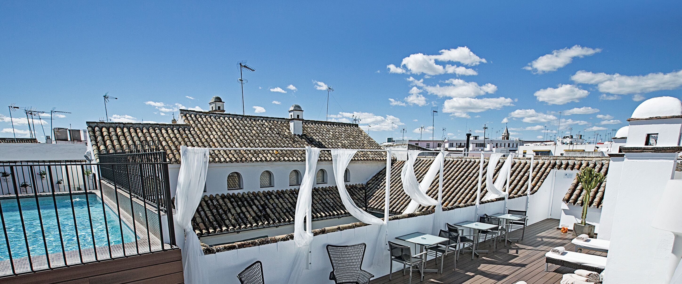 A rooftop pool area with a clear view of the city skyline, including buildings with domed roofs and a church spire.
