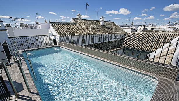 A rooftop swimming pool with a tiled deck and a view of surrounding buildings.