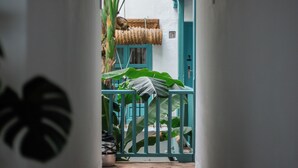 A narrow hallway with a tiled floor, leading to a room with a green door and a thatched roof.