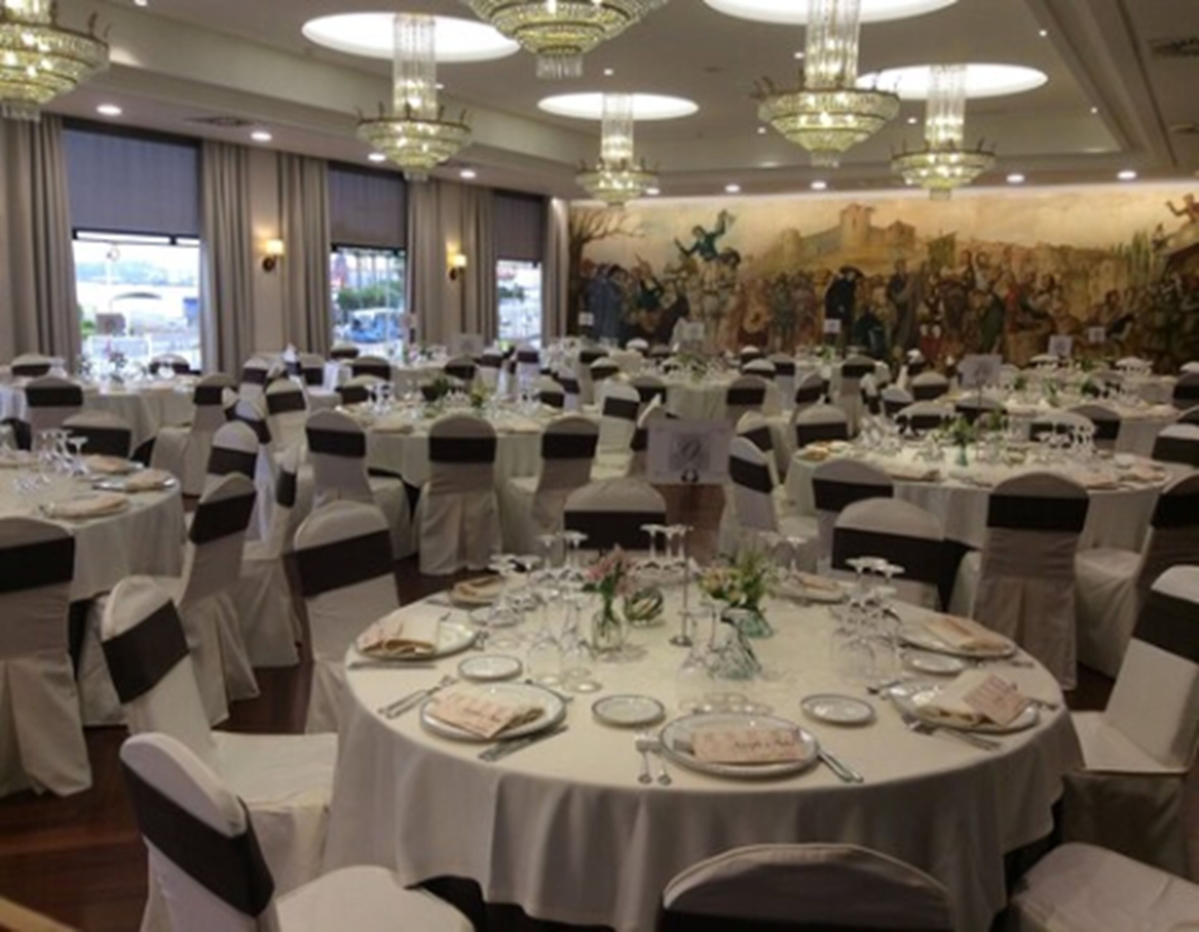 A banquet hall with round tables set for dining, adorned with white tablecloths and black sashes.