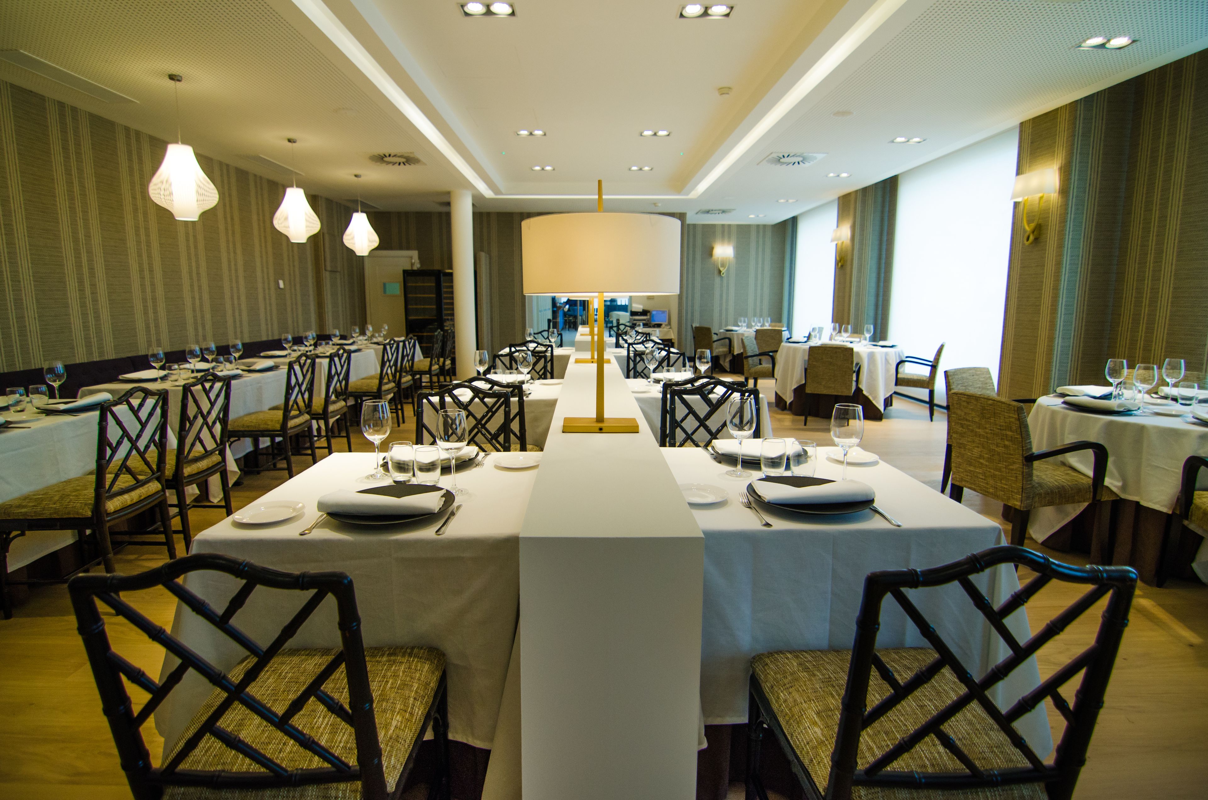 Een ruime eetzaal met meerdere gedekte tafels, stoelen en verlichting van het plafond.