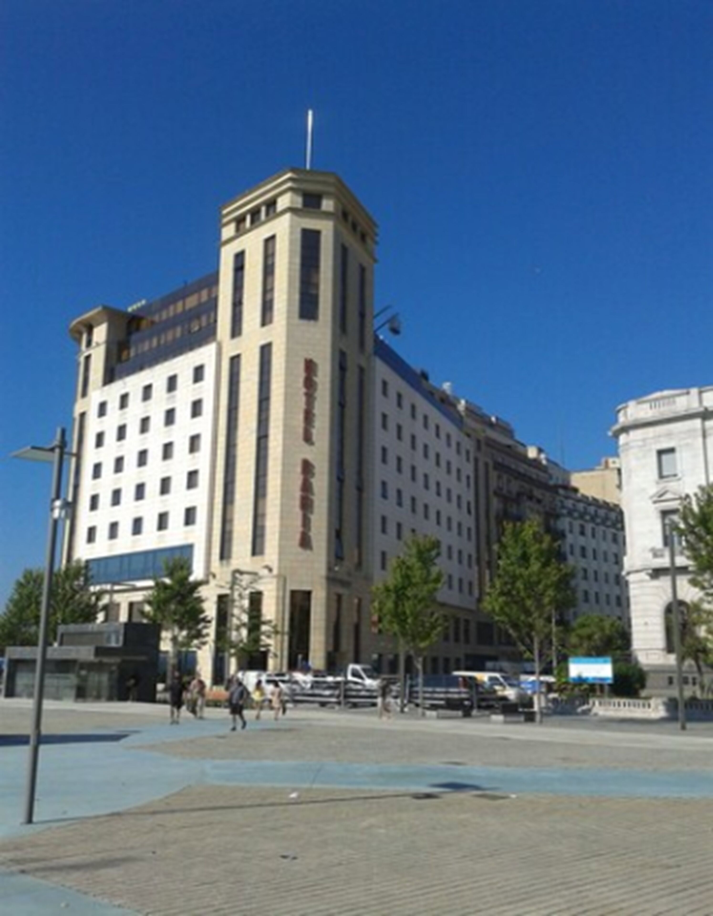 A large, multi-story hotel with a prominent central tower, wide pedestrian pathways, and a clear blue sky.