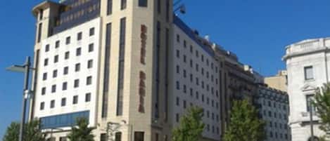 A large, multi-story hotel with a prominent central tower, wide pedestrian pathways, and a clear blue sky.