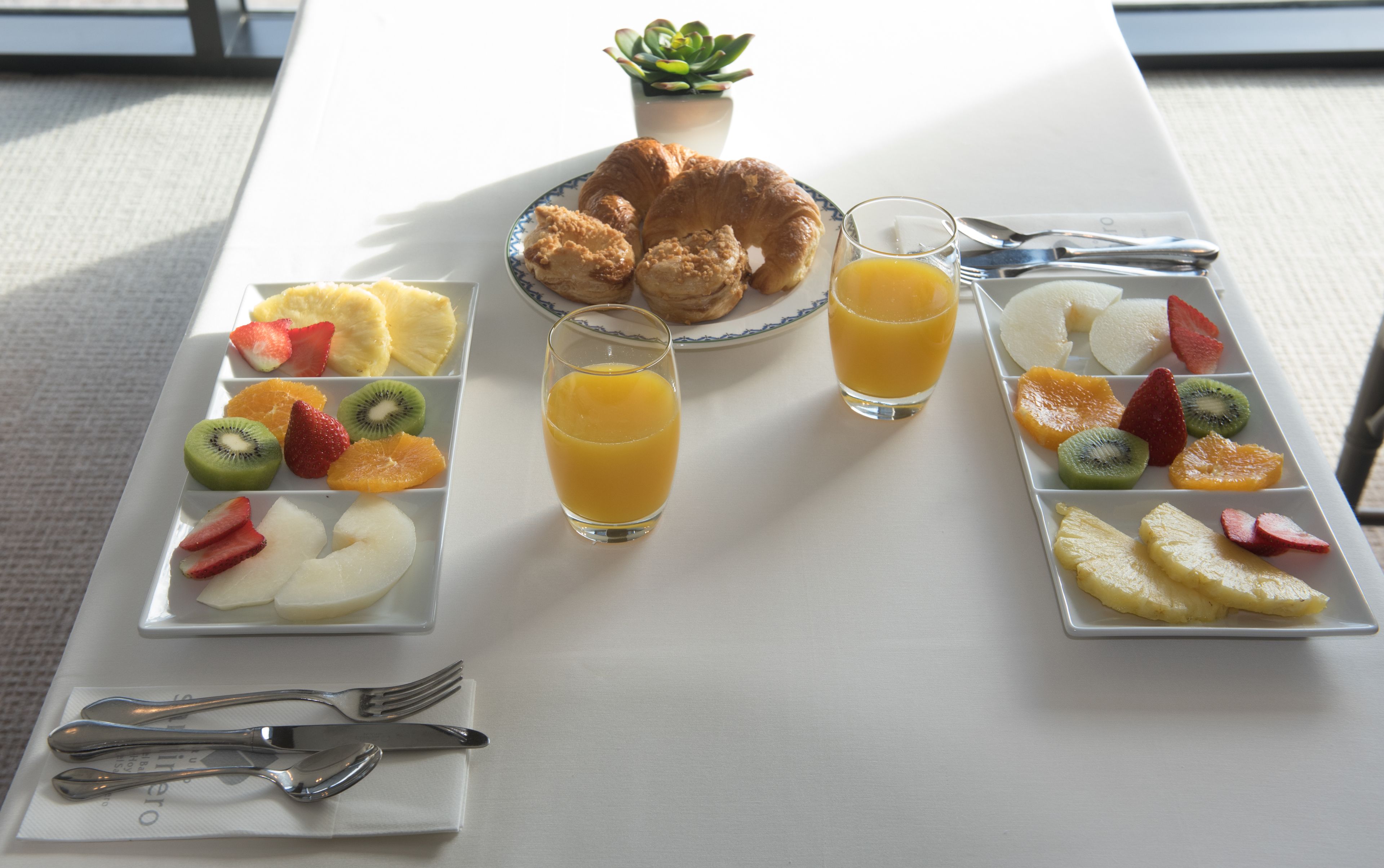 Een ontbijttafel met croissants, fruit en sinaasappelsap.
