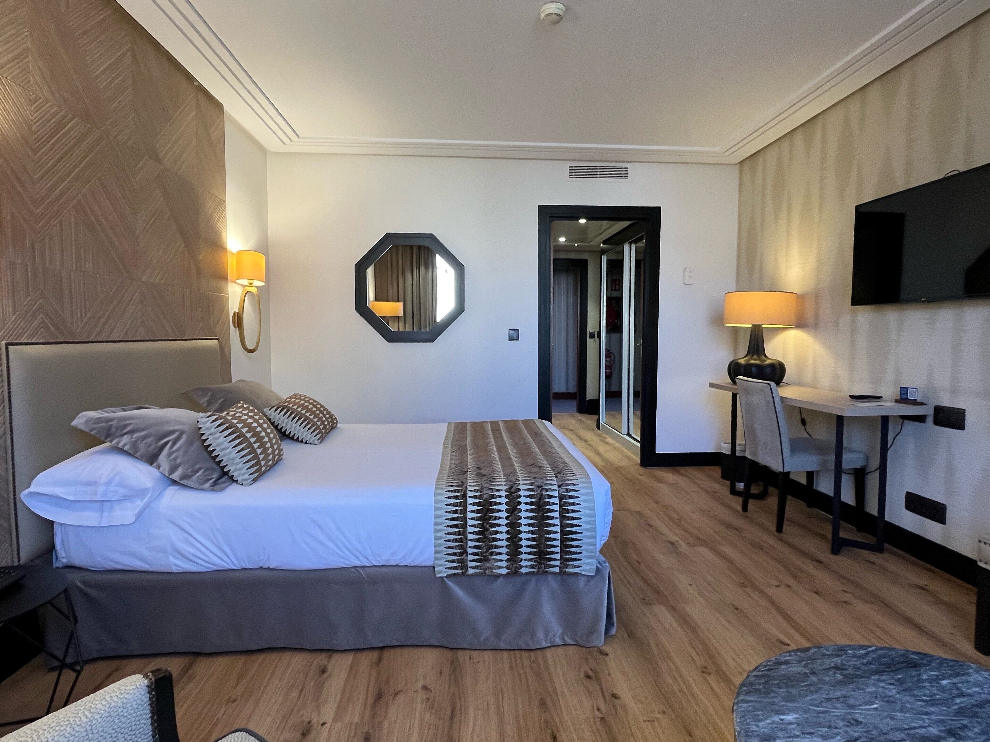 A hotel room with a large bed, bedside lamps, a desk with a chair, and a television.