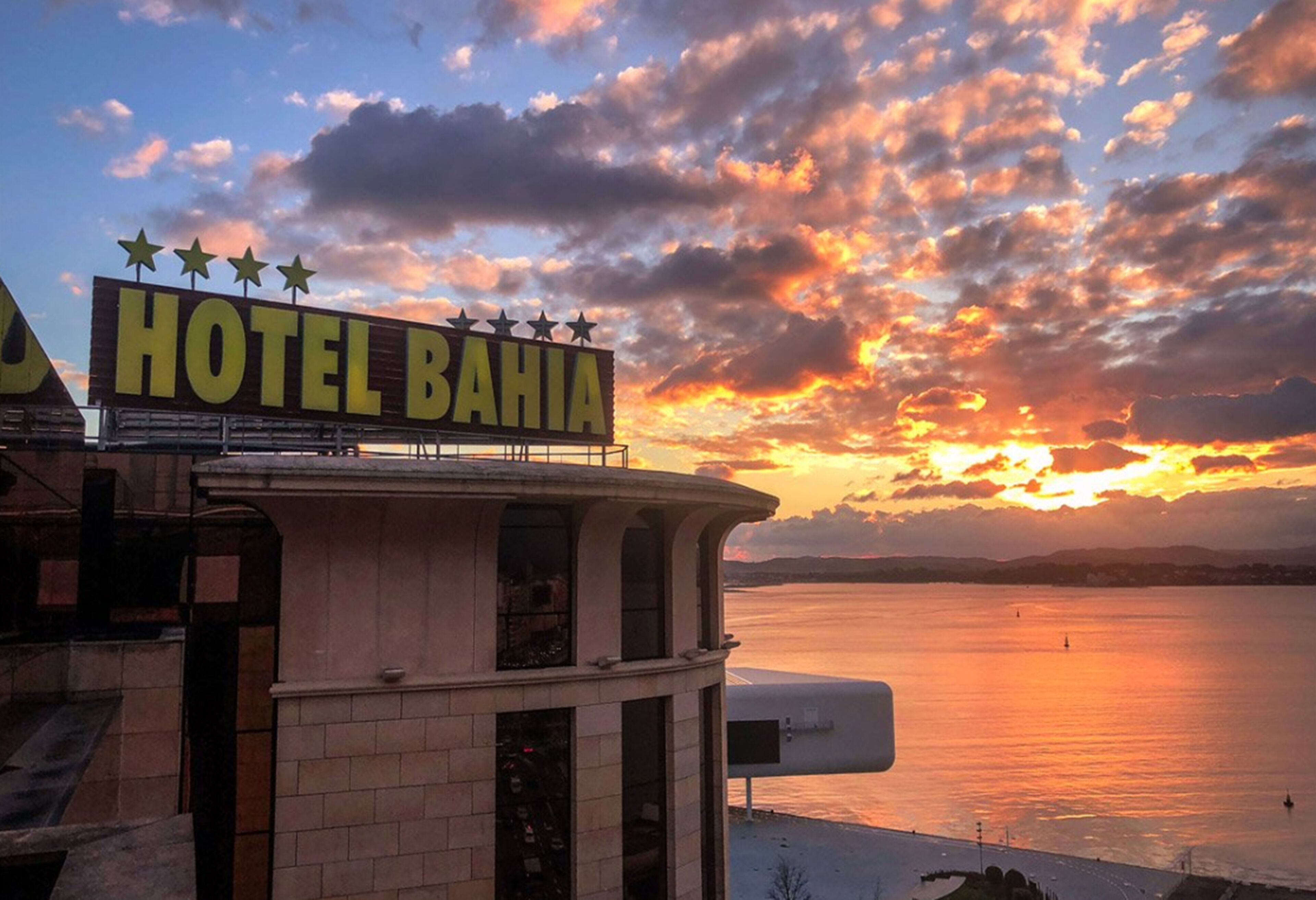 Un letrero de hotel con cinco estrellas y el nombre "HOTEL BAHIA" sobre un fondo de atardecer.