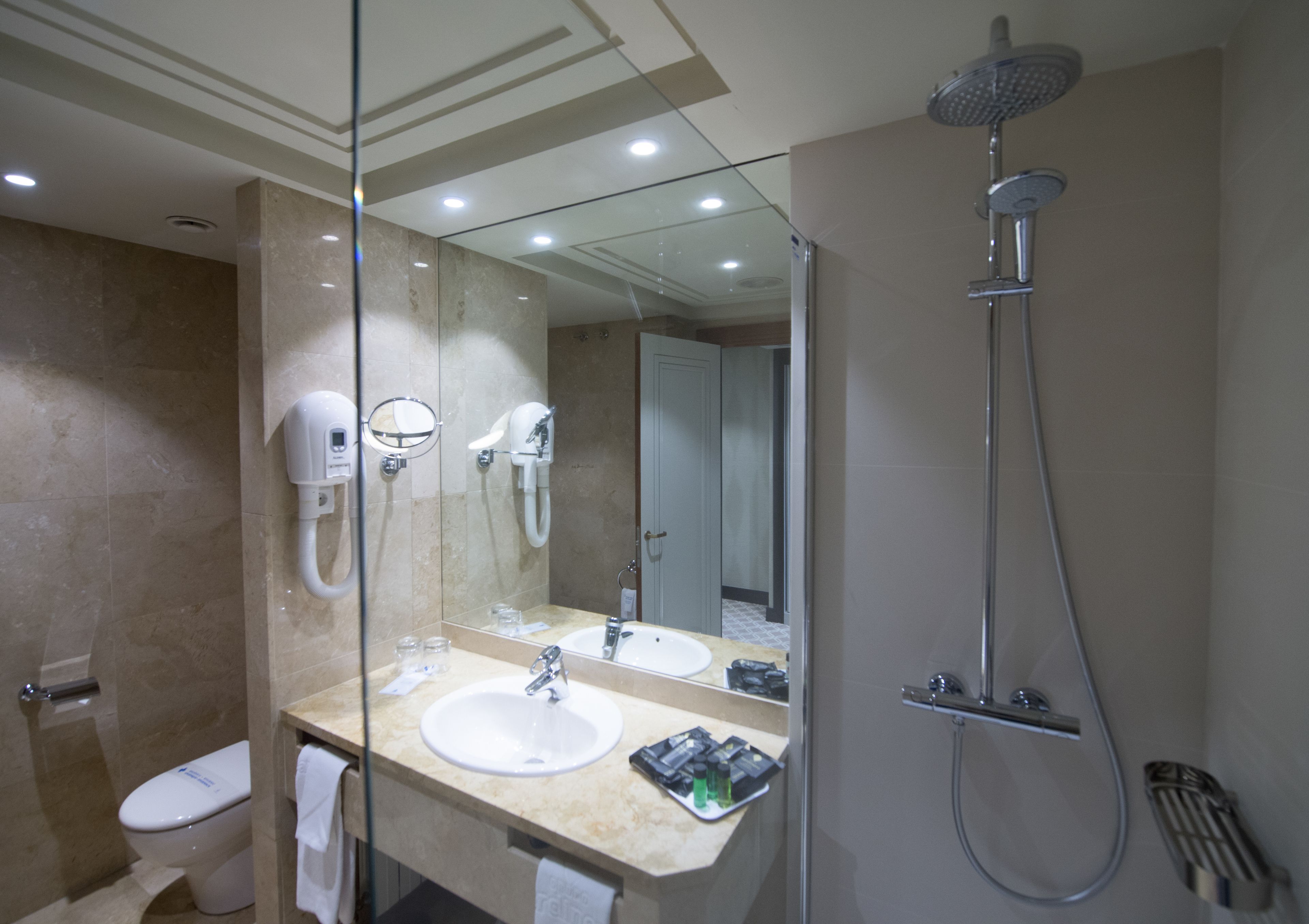 Un baño moderno con tocador con vidrio, ducha e inodoro.
